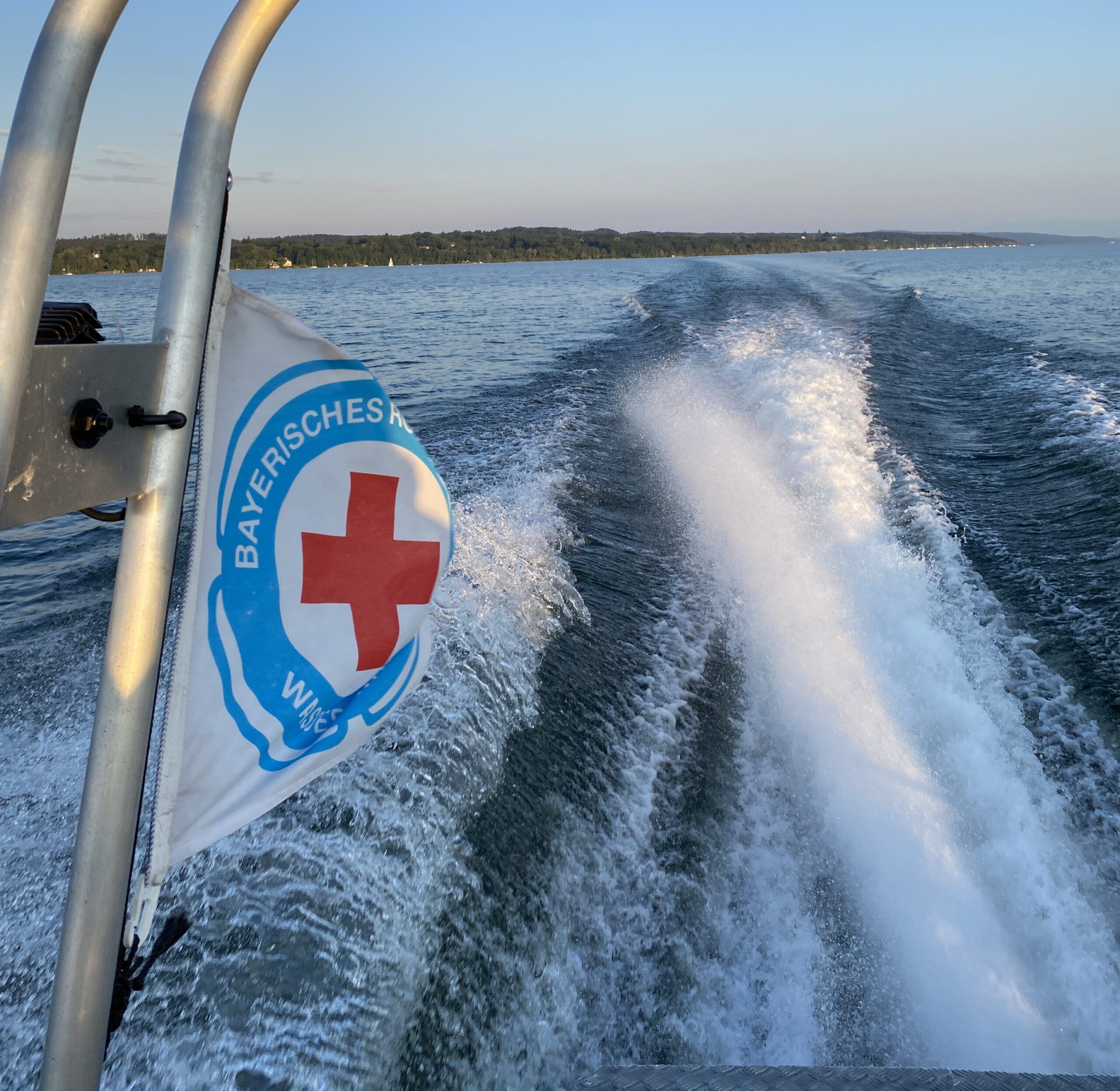 Symbolbild: Motorrettungsboot der Wasserwacht auf Einsatzfahrt auf dem Ammersee. Blick achteraus auf die wehende WW Fahne vor dem Horizont